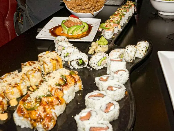 Variety of sushi rolls arranged on a black table with sauces, avocado, and garnishes in a restaurant setting.