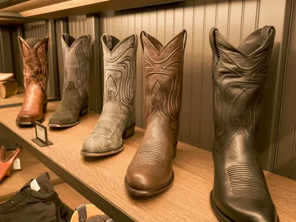 Row of six cowboy boots in various shades displayed on a wooden shelf against a paneled wall.