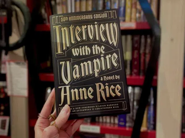 Hand holding the 50th Anniversary Edition of Interview with the Vampire by Anne Rice with overlaid text on the book cover.