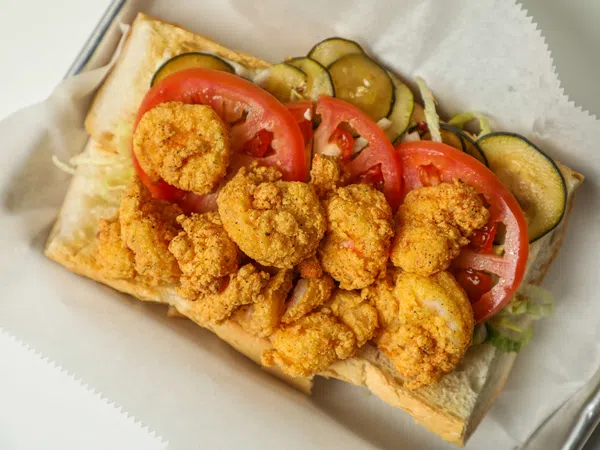 Fried shrimp po'boy sandwich with sliced tomatoes, pickles, and lettuce on a sub roll.