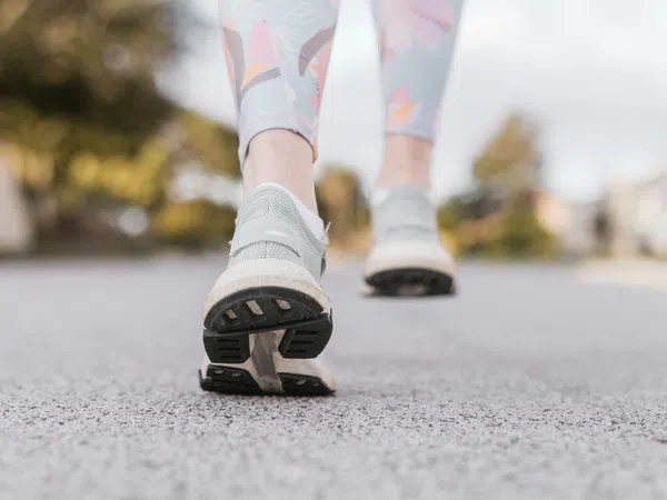 Close-up of a person walking on pavement wearing gray running shoes and floral leggings outdoors.