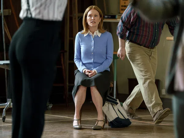 Woman in blue cardigan and black skirt sitting on a chair surrounded by blurred walking people indoors