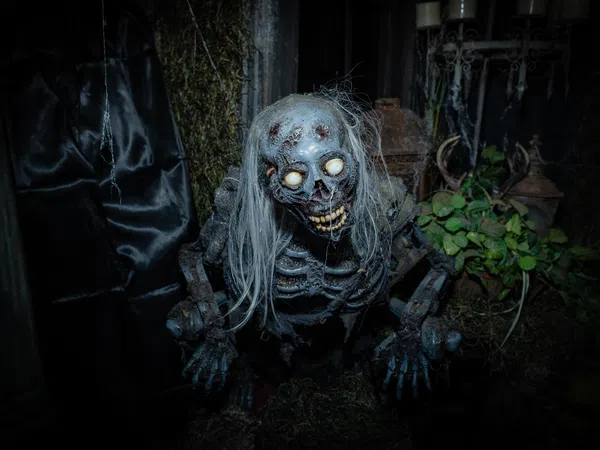 Creepy skeleton figure with glowing eyes and long white hair in a dark, eerie setting with plants and moss.