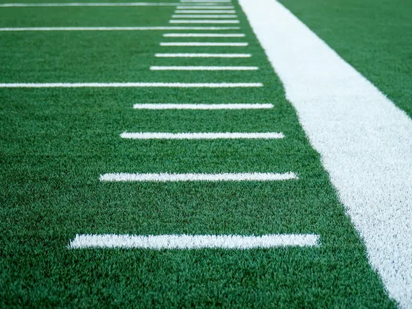 Close-up of green turf with white yard lines on an American football field.