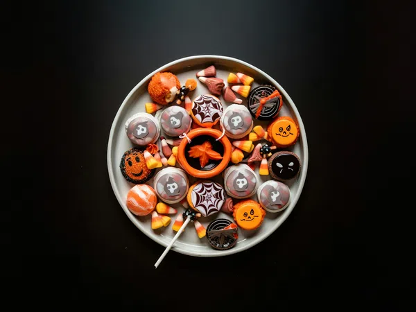 Plate of Halloween-themed cookies and candy corn on black background with orange and black decorations