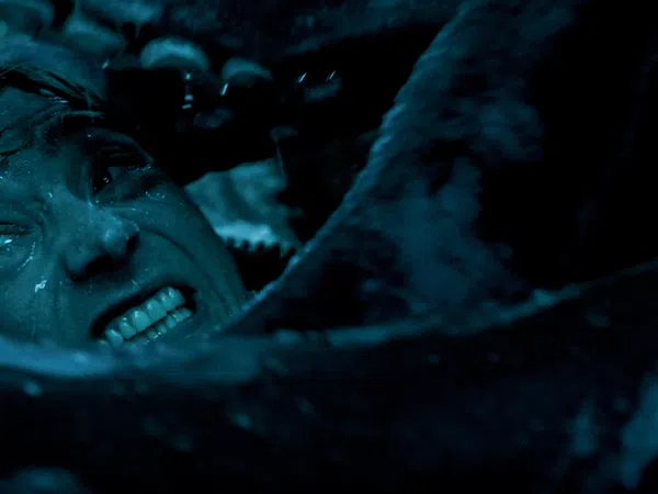 Close-up of a man's tense face underwater surrounded by tentacles in dark blue lighting.