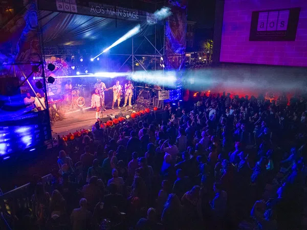 Live band performing on AOS Main Stage with colorful lights and large crowd at night concert event.