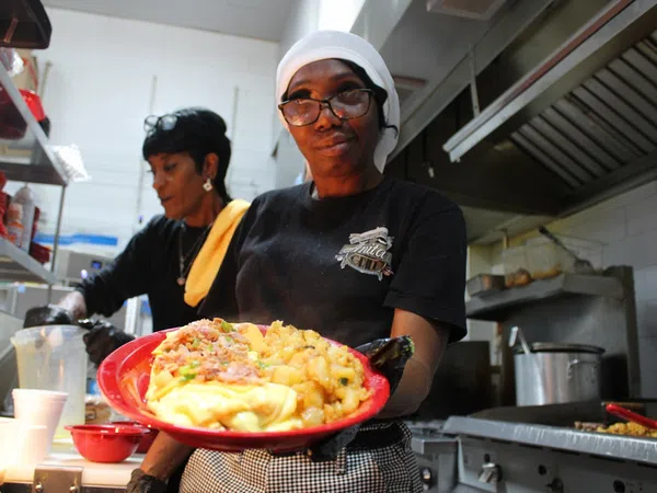 Smiling chef in kitchen holding a red plate with breakfast food including eggs, potatoes, and bacon.