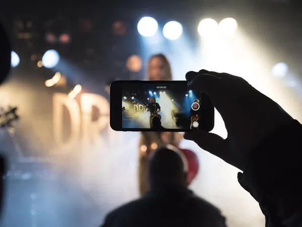 Person recording a live music performance on smartphone with stage lights and smoke effects in background