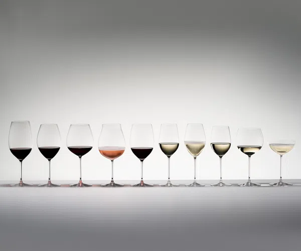 Row of ten wine glasses with varying shapes filled with red, rosé, and white wine against a white background.