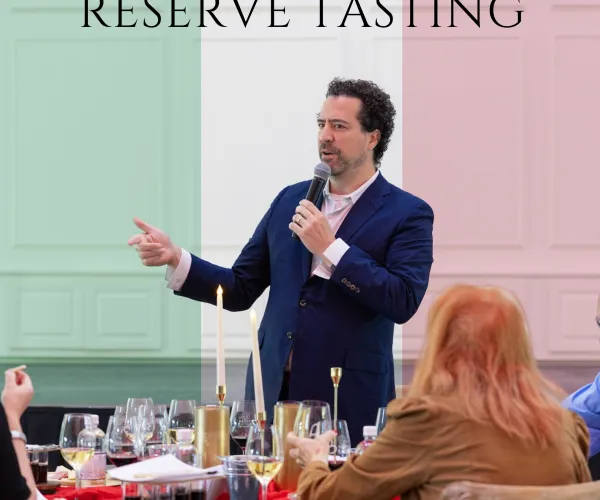 Man speaking at Italian wine reserve tasting event with attendees seated at table with wine glasses.