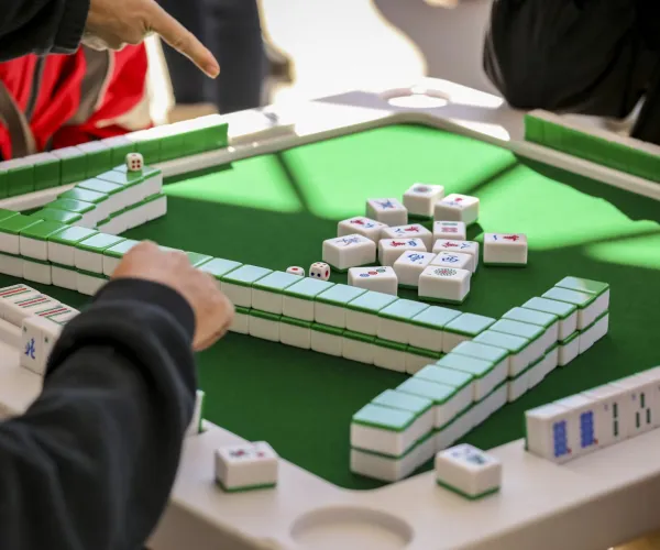 People playing Mahjong on a green felt table with tiles arranged and dice in the center during a game.