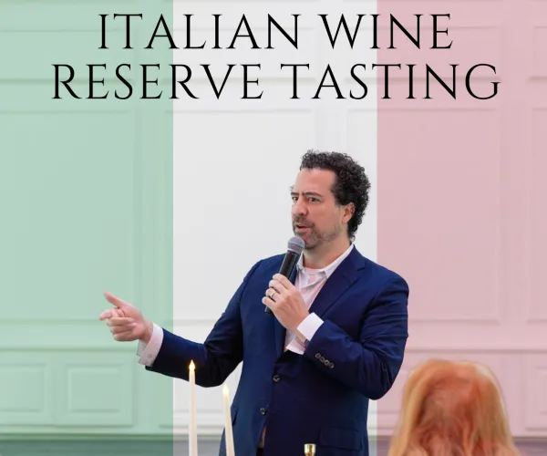 Man speaking at Italian wine reserve tasting event with attendees seated at table with wine glasses.