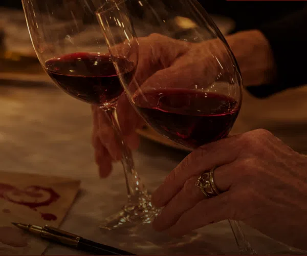 Two hands clinking wine glasses over a table with mysterious notes and dim candlelight ambiance