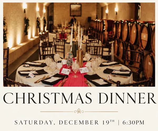 Elegantly set Christmas dinner tables with candles and wine barrels in cozy festive wine cave setting.