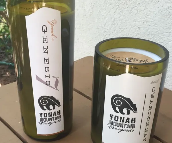 Green glass candles from Yonah Mountain Vineyards with Genesis and Chardonnay labels on a wooden table.