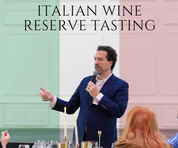 Man giving a speech about Italian wine reserve tasting with guests seated at a table with wine glasses.