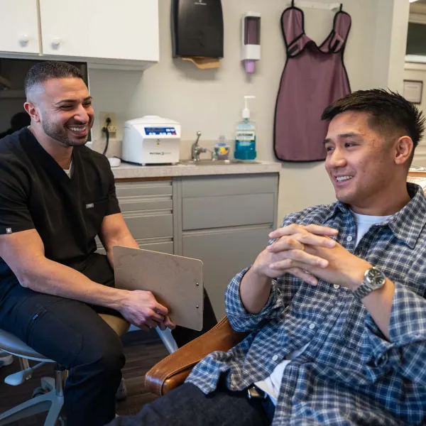 Dentist in black scrubs consulting with a smiling male patient sitting in a dental chair in a clinic.