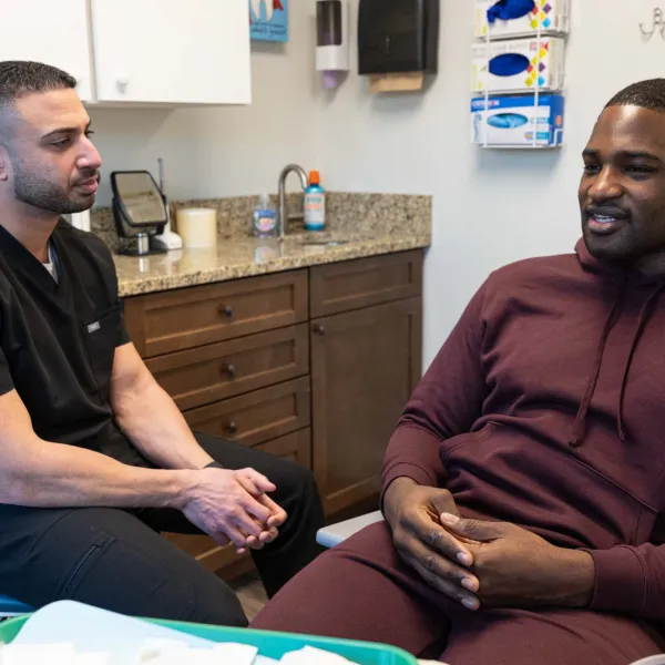 Dentist in black scrubs consulting a male patient in a burgundy Nike hoodie in a modern dental office.