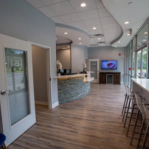 Modern dental office reception area with curved stone desk, wood floor, and large windows with bar stools.