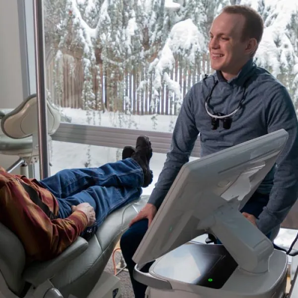 Dentist consulting and smiling at elderly male patient in a bright clinic with snowy landscape outside window