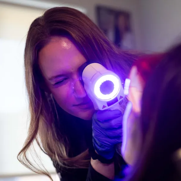 Healthcare professional using a dermatoscope to examine a patient's skin under bright light in a clinical setting