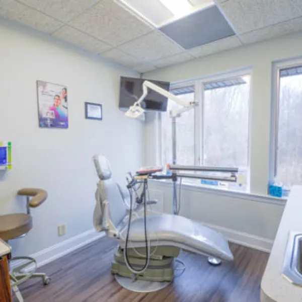 Bright dental clinic room with modern chair, equipment, large window, and clean wooden floor.