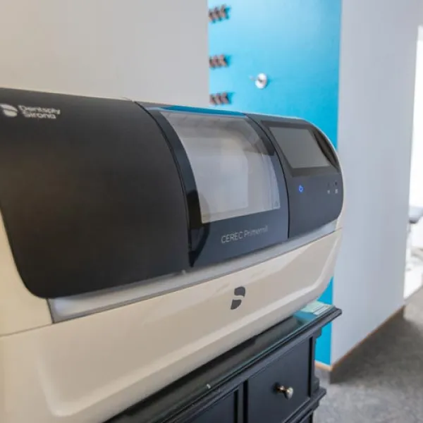 CEREC Primescan dental milling machine on a black cabinet in a modern dental office corridor.