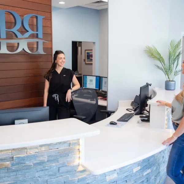 Reception area with smiling receptionist and client at curved white desk in modern office lobby.