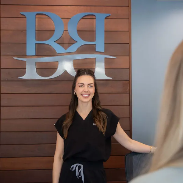 Smiling woman in black uniform standing in front of wooden wall with silver RRH logo in office setting