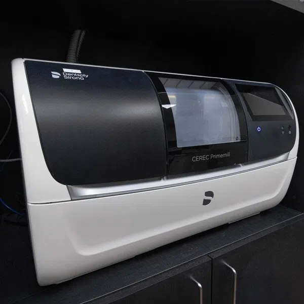 Dentsply Sirona CEREC Primemill dental milling machine in black and white on a dark cabinet.