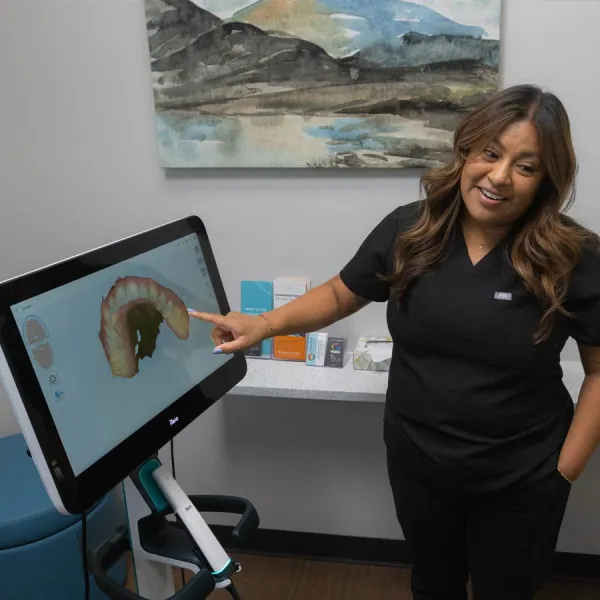 Dental professional pointing at 3D digital dental model on screen in modern dental office.