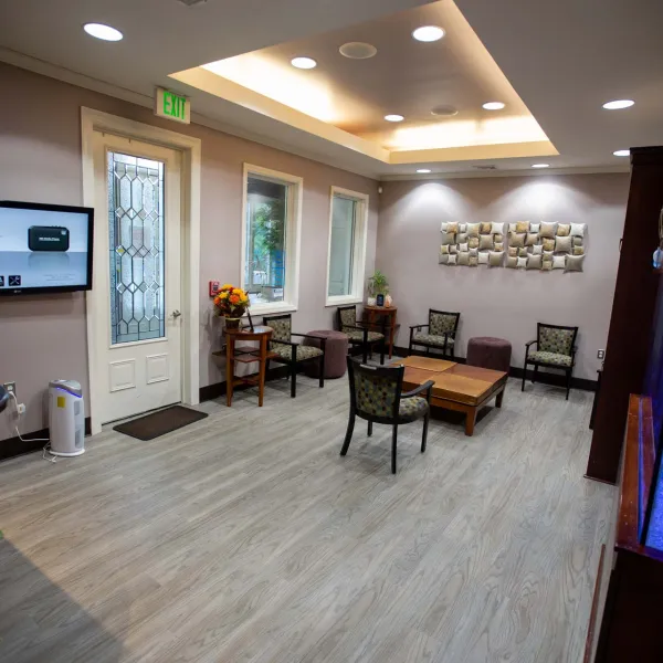 Modern waiting room with chairs, wooden table, wall art, aquarium, and television screen near entrance door.