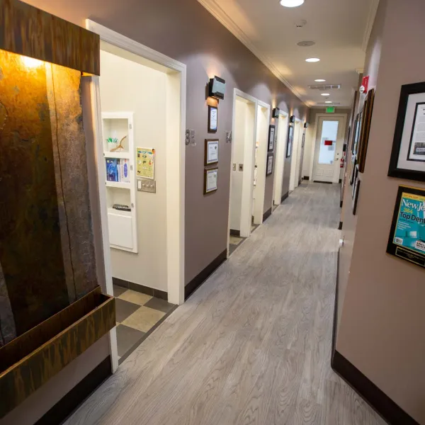 Well-lit dental office hallway with open patient rooms and framed awards on beige walls.