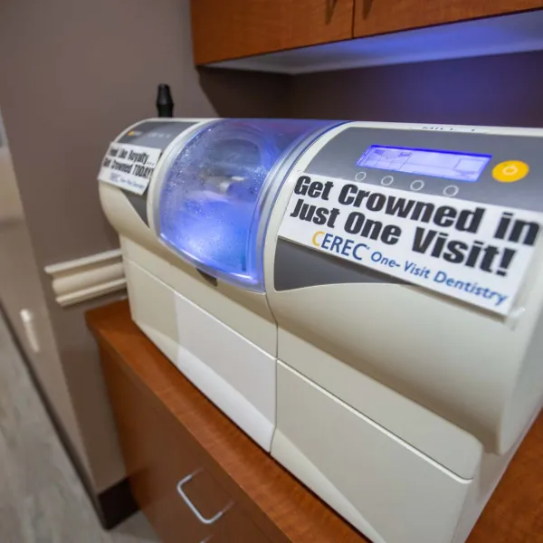 CEREC dental machine in office with sign promoting same-day crown services in one visit.