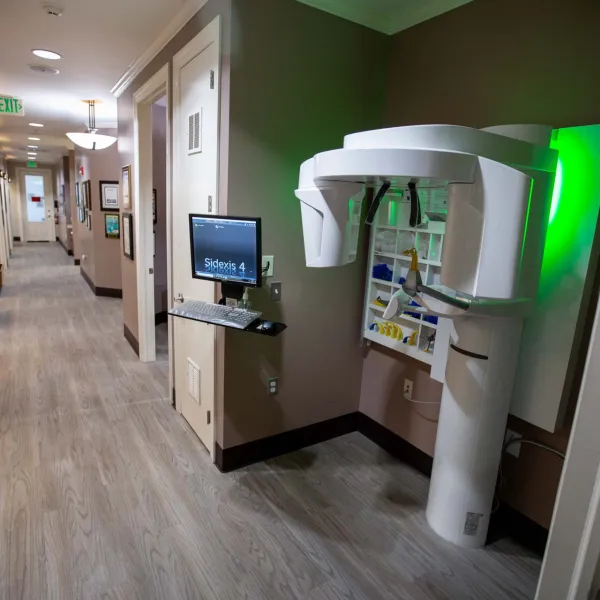 Dental office hallway with a panoramic dental X-ray machine and computer workstation on the wall.