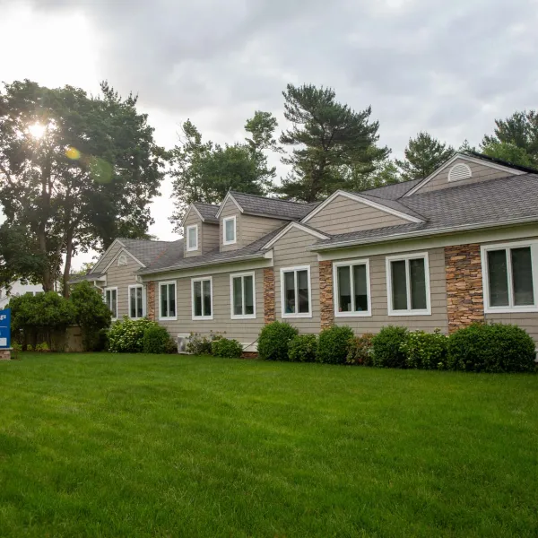 Modern single-story building with stone and siding exterior surrounded by green lawn and trees under cloudy sky.