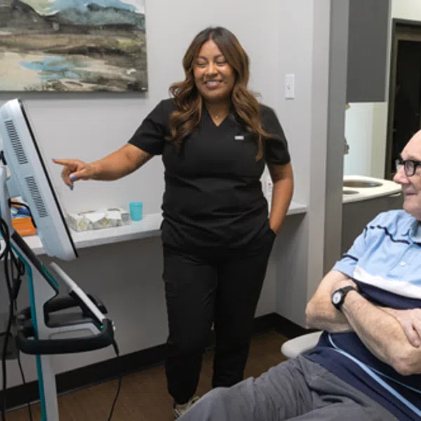 Healthcare worker in black scrubs showing information on a monitor to a seated elderly patient in a medical office