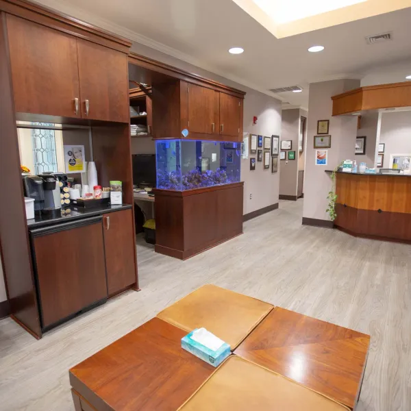 Waiting room with wooden furniture, fish tank, coffee station, and reception desk in a professional office.