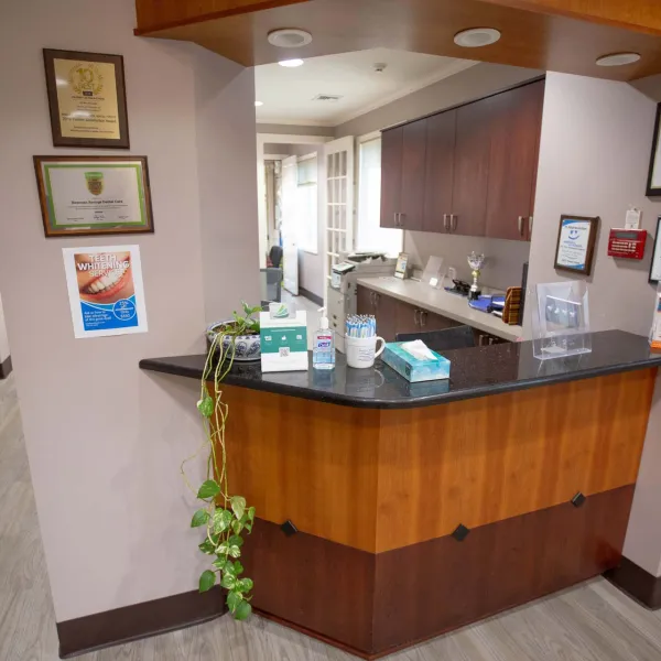 Reception desk area with wood paneling, granite countertop, certificates on beige walls, and office supplies in dental clinic.