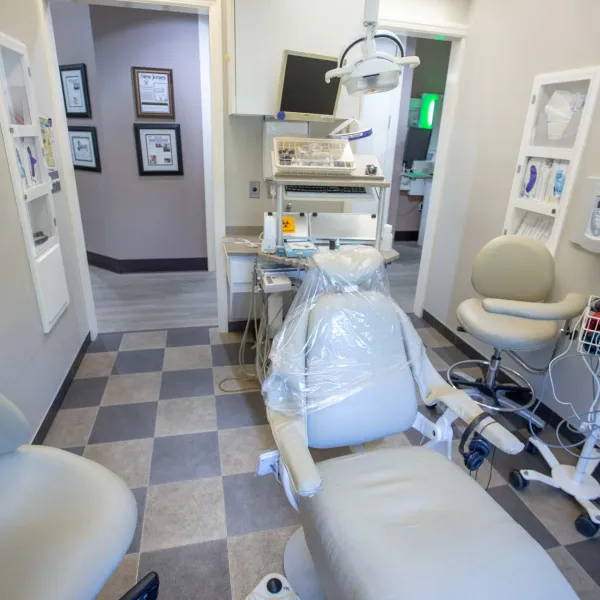 Clean dental exam room with patient chair, medical equipment, and bright lighting on checkered floor.