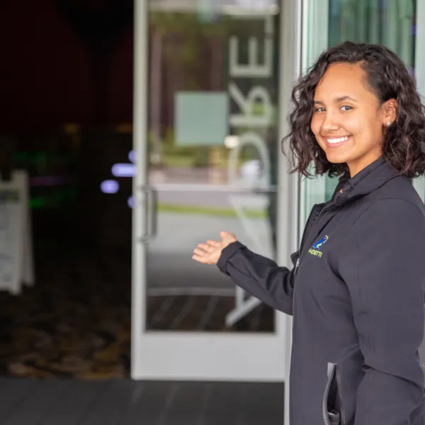 Smiling staff member welcoming guests at an entrance, showcasing hospitality in a vibrant environment.
