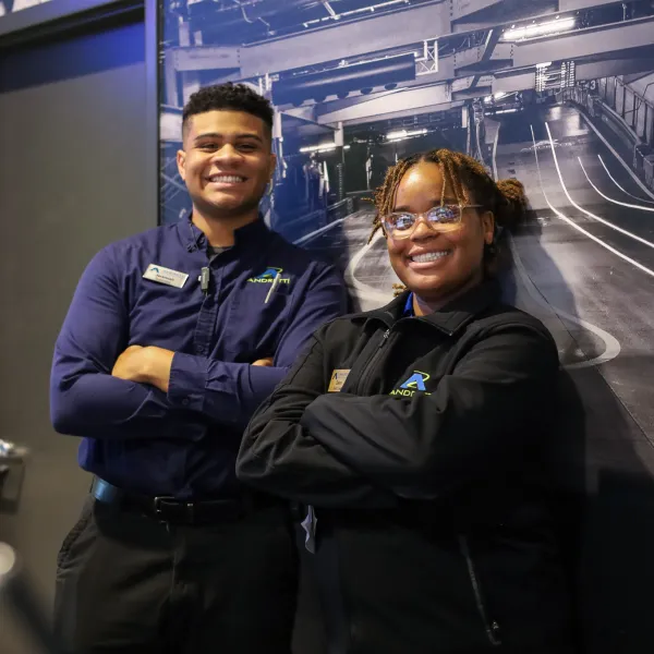 Two smiling employees posing confidently in a modern work environment with industrial decor.