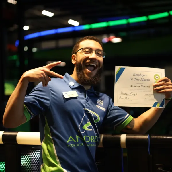 Happy employee holding Employee of the Month certificate, celebrating at a vibrant indoor sports venue.
