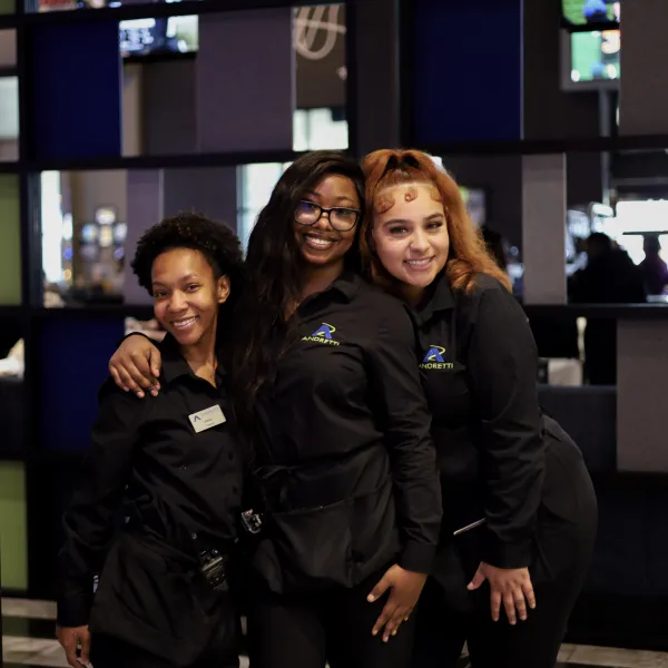 Three smiling female employees in black uniforms posing together inside a modern establishment with colorful wall panels.