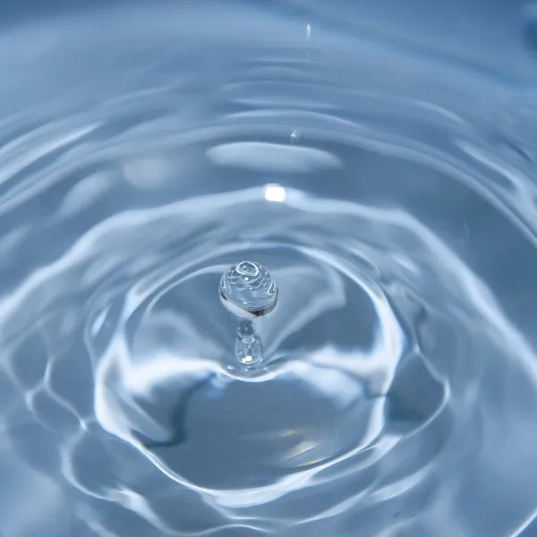 Close-up of a water droplet creating ripples on a clear blue water surface in soft lighting