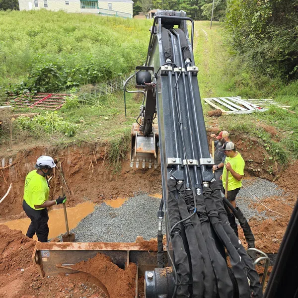 Construction workers in neon shirts operating excavator and preparing foundation with gravel in a dirt trench