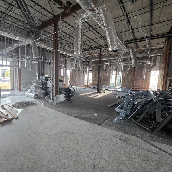 Interior view of a commercial space under construction with exposed ducts, metal studs, and construction materials scattered