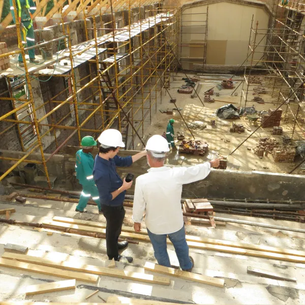 Construction site with workers and two supervisors in hard hats inspecting scaffolding and building progress.
