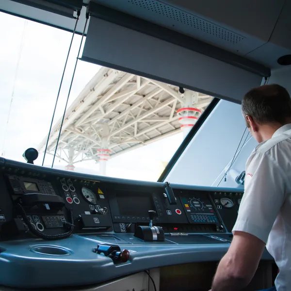 Train driver operating controls inside a modern locomotive cabin with a view of station platform roof.